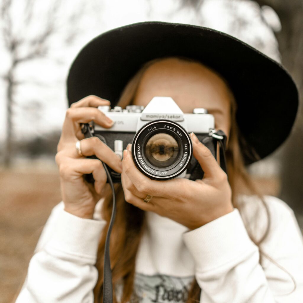 Stylish woman in black hat holding a vintage camera outdoors during fall.