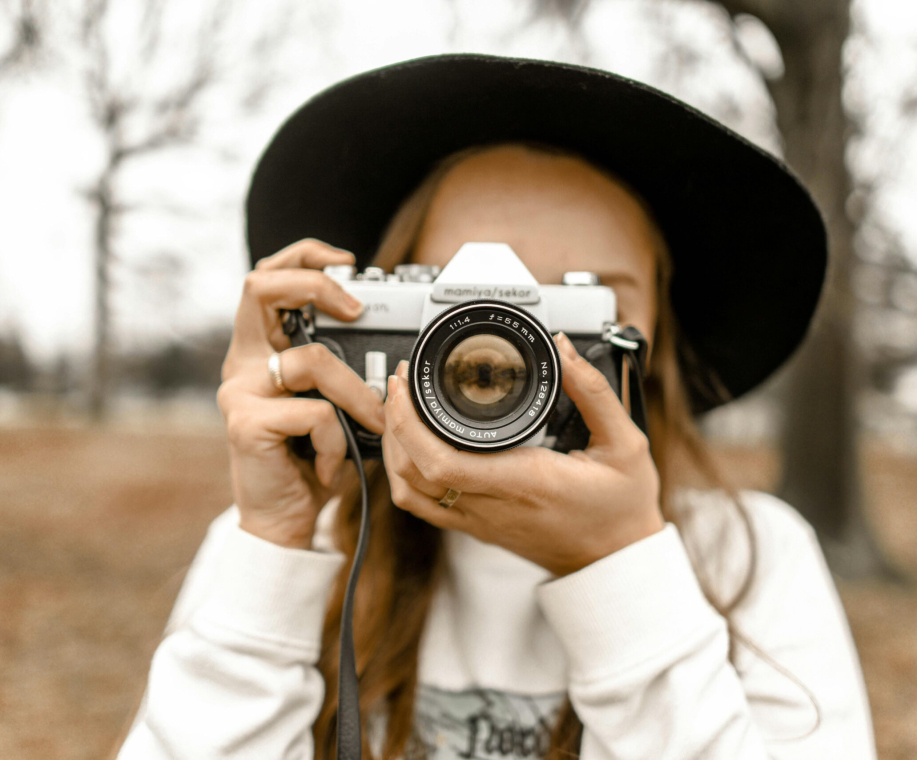 Stylish woman in black hat holding a vintage camera outdoors during fall.