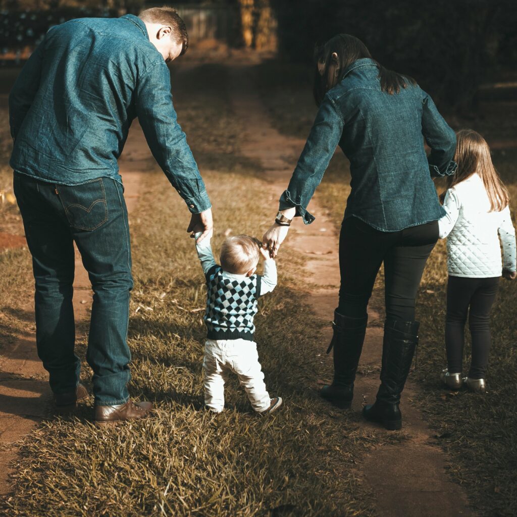 pexels-photo-1682497-1682497-1 A family of four walks hand in hand on a path, enjoying a sunny day outdoors.