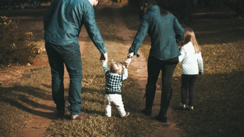 A family of four walks hand in hand on a path, enjoying a sunny day outdoors.